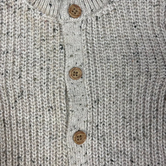 Grauer Overall aus Strick mit Holzknöpfen auf hellgrauer Unterlage – detail