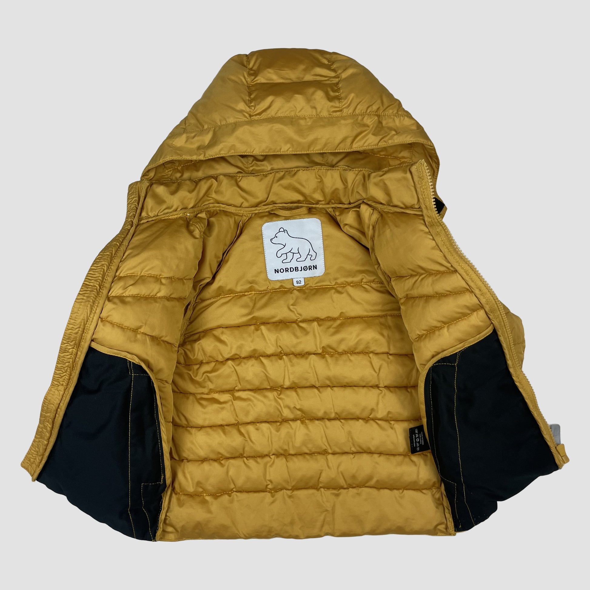 Senfgelbe Kinder-Steppjacke von Nordbjørn mit Kapuze, Reißverschluss und reflektierenden Details. – front