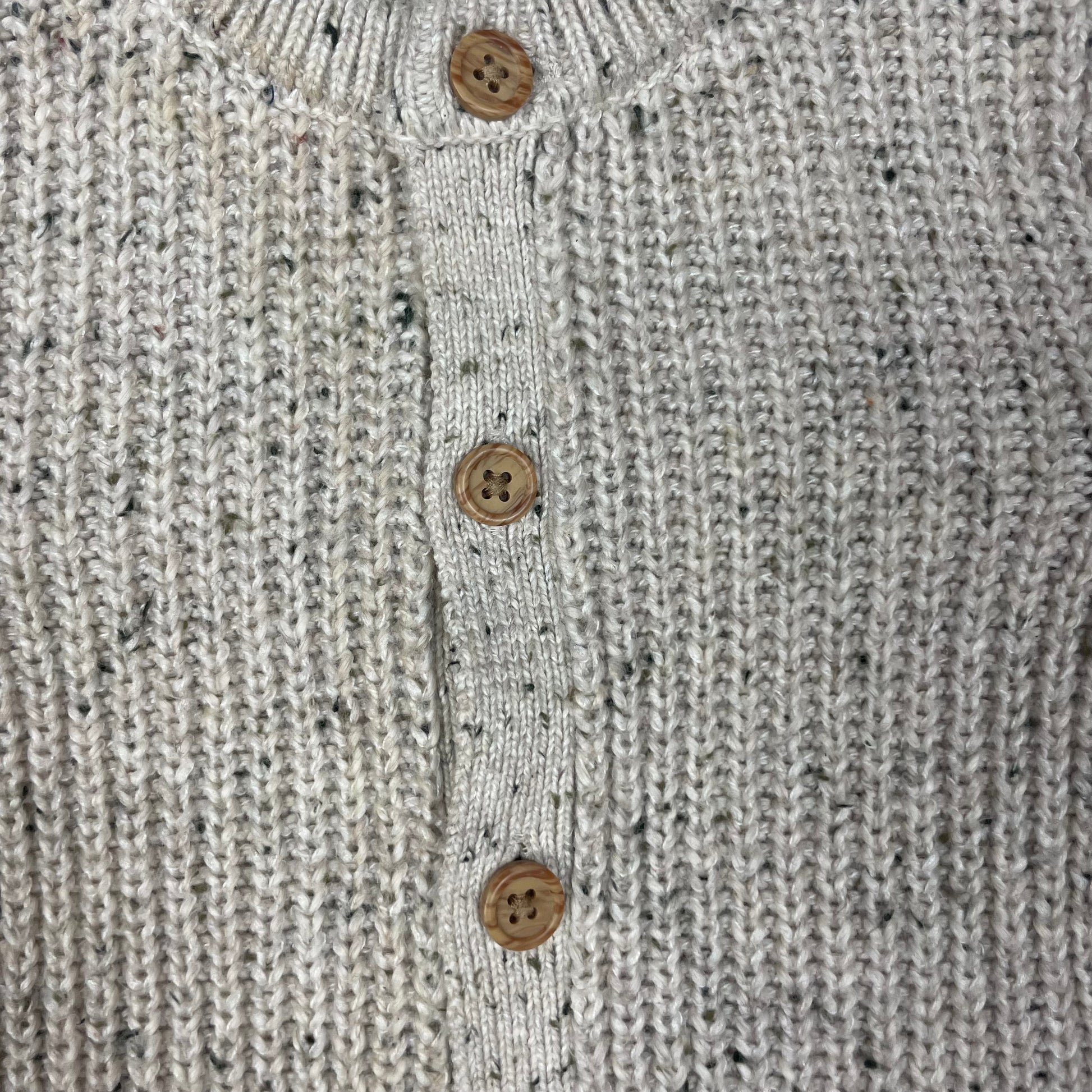 Grauer Overall aus Strick mit Holzknöpfen auf hellgrauer Unterlage – detail