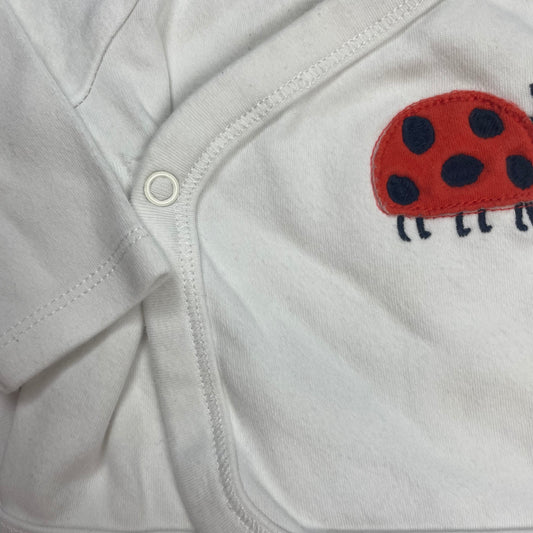Weißer Baby-Kimono mit Marienkäfer-Applikation auf der Vorderseite – close‑up