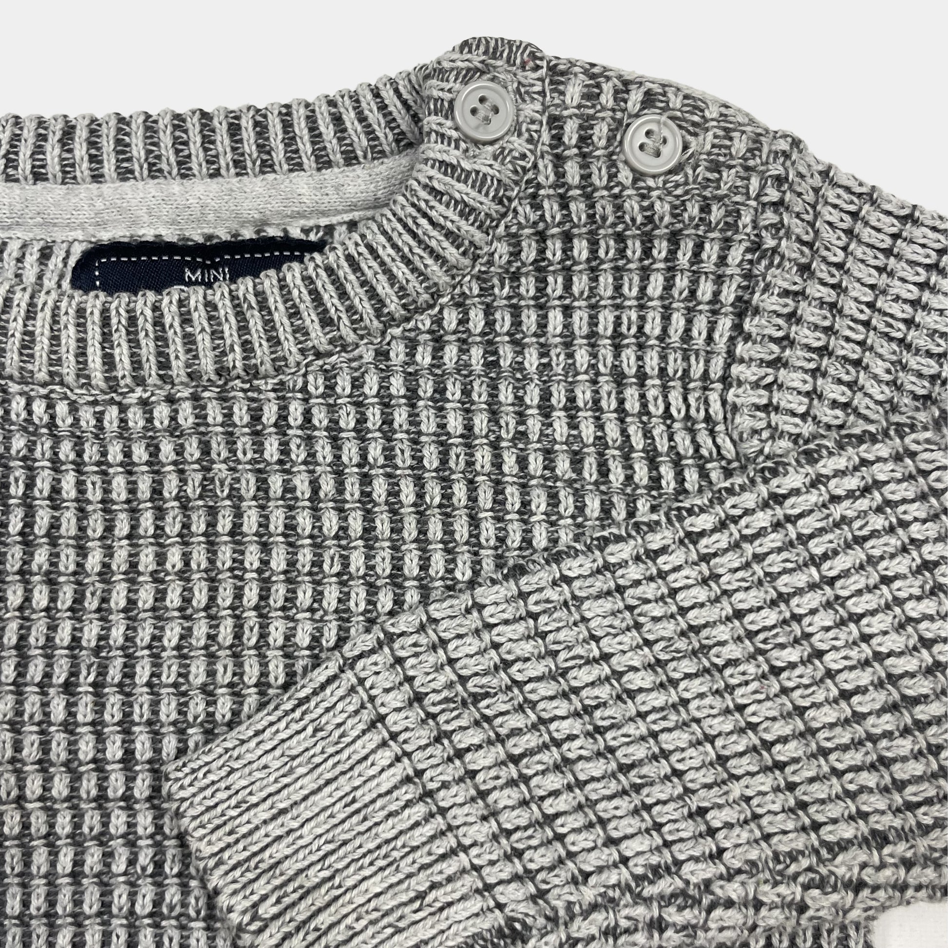 Grauer Strickpullover mit Knöpfen auf der Schulter, Größe 6-9 Monate. – detail