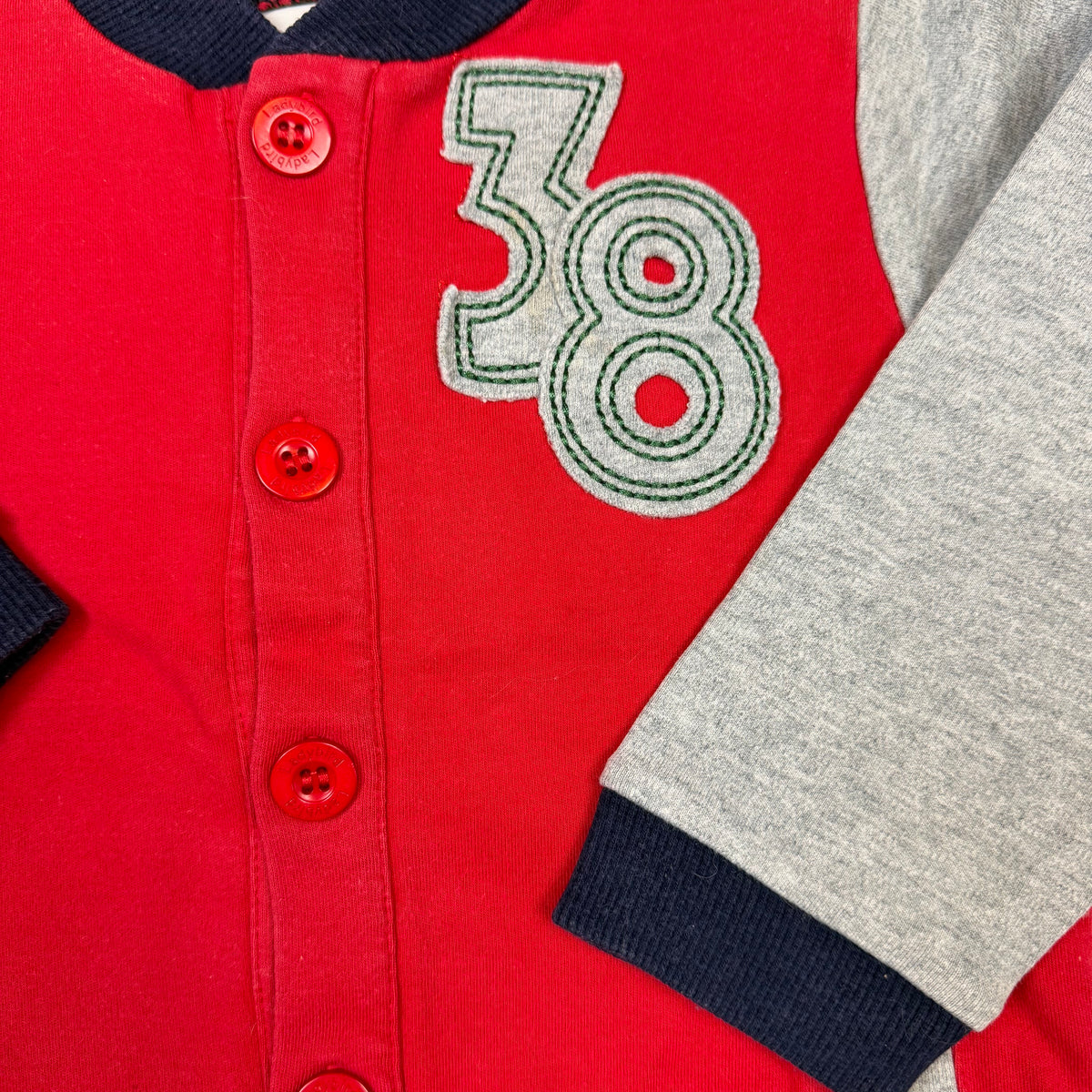 Rote Sweatjacke für Kinder mit grauen Ärmeln, Druckknöpfen und 38-Applikation – detail