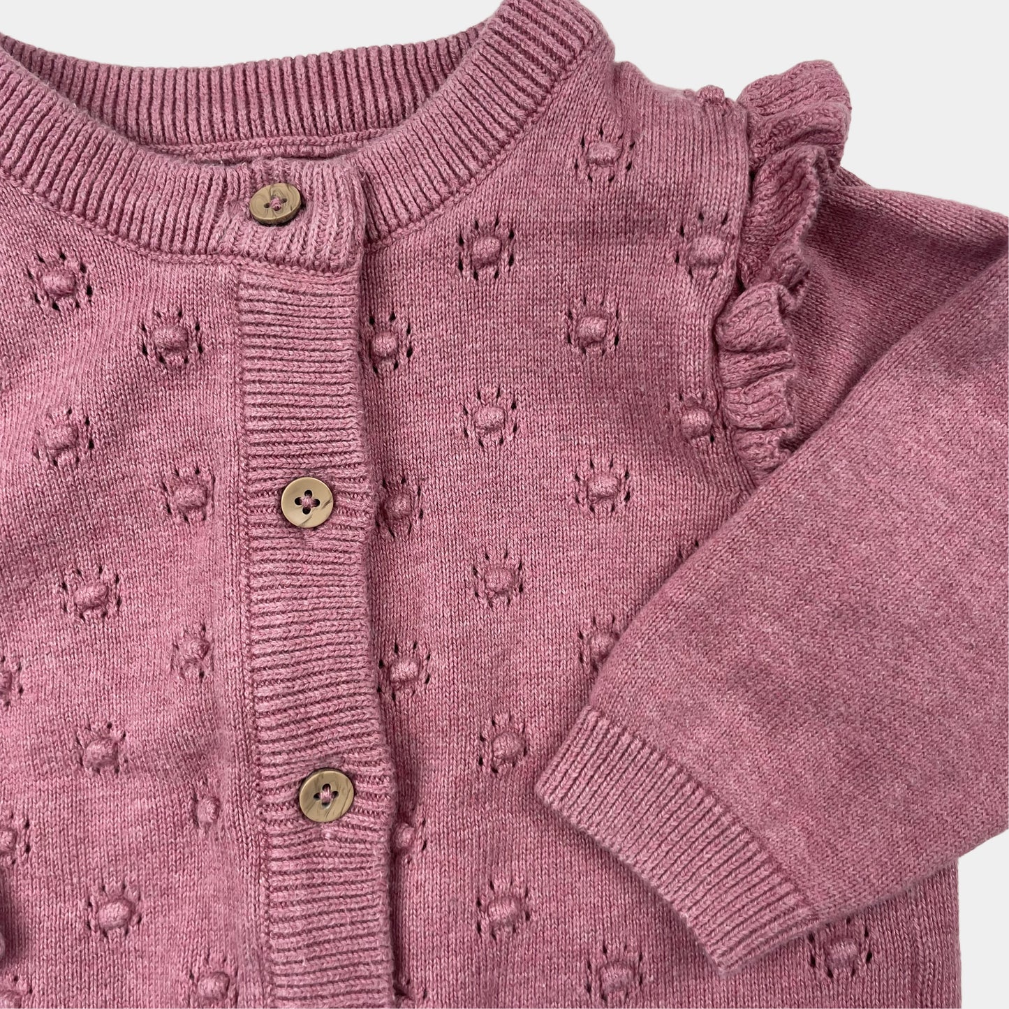 Lilafarbene Strickjacke für Babys mit Rüschen an den Schultern. – detail