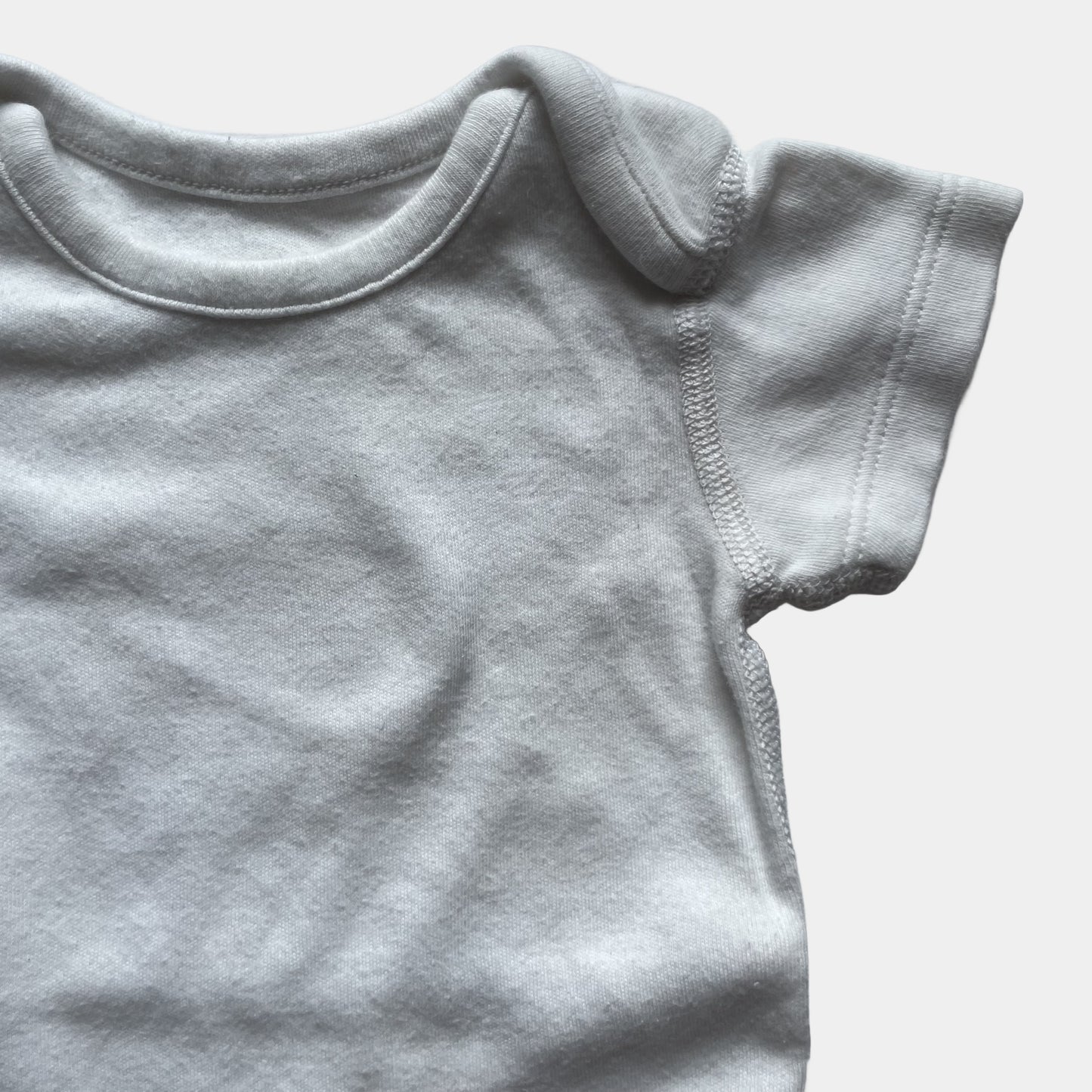 Weißer Babybody aus Baumwolle mit kurzen Ärmeln und Druckknöpfen im Schritt. – detail